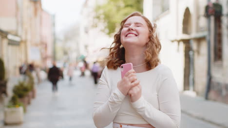 Young-woman-use-mobile-smartphone-celebrating-win-good-message-news-outdoors-in-urban-city-street