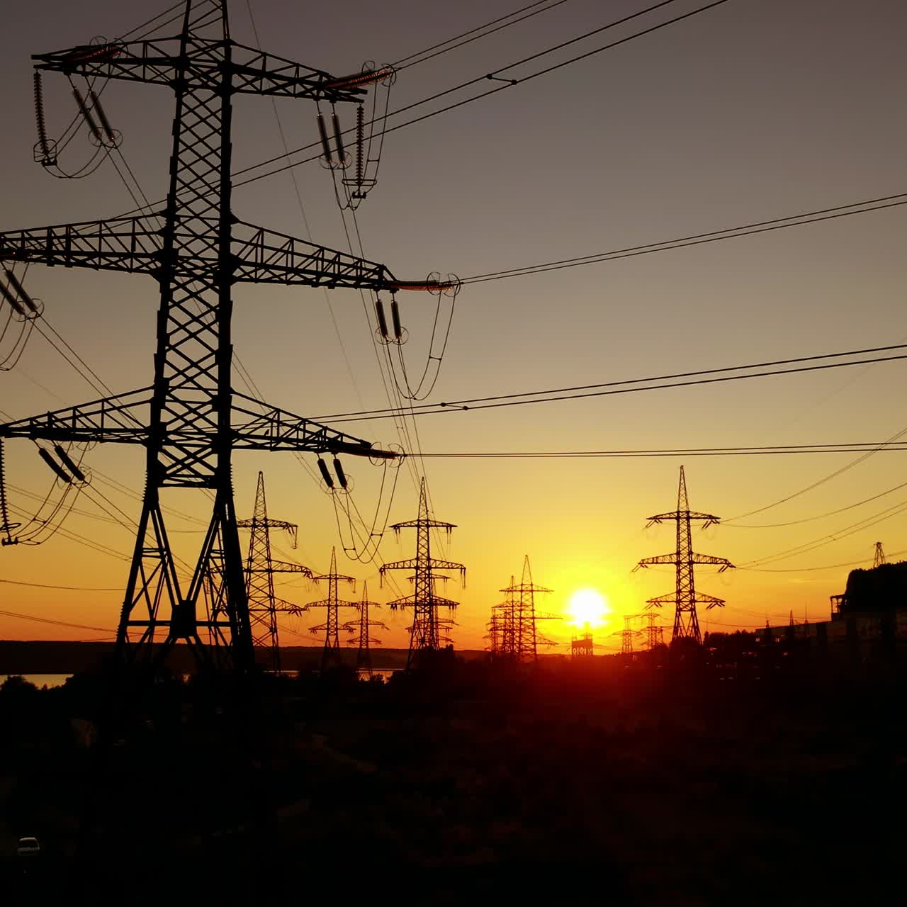 Transmission electric on towers at sunset. High-voltage power lines. Electrical pylons on the orange sky background. Drone view. Camera rising up.