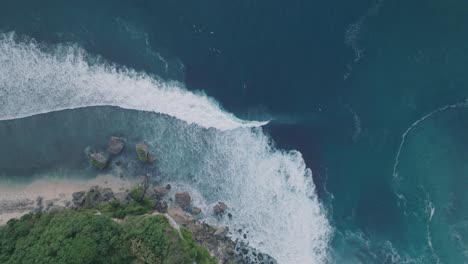 Drone-De-Arriba-Hacia-Abajo-De-Surfistas-No-Identificables-Al-Atardecer-Con-Agua-Azul-Profunda-Y-Dorada-Y-Costa-En-Padang-Padang,-Bali,-Uluwatu-Indonesia