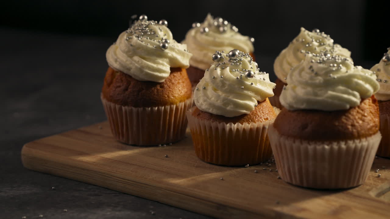 Delicious frosted cupcakes on a wooden tray, perfect for dessert display as sprinkles are dropped over tops on frosting
