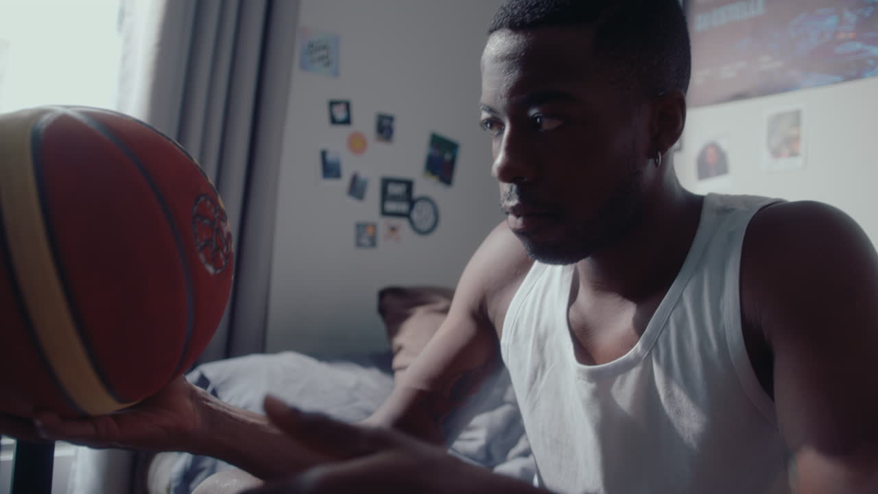 Young Black Guy Sitting in Bedroom and Playing with Basketball