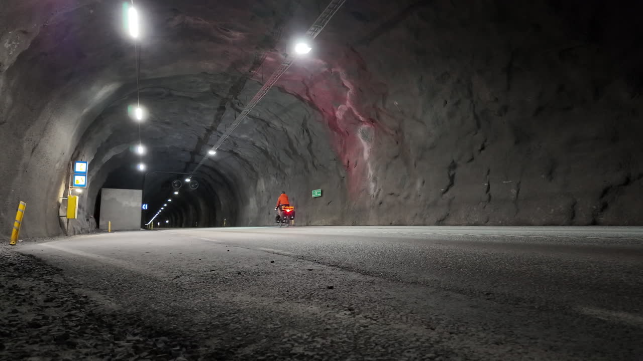 Cyclist traversing the dimly lit 5900m Fáskrúðsfjarðargöng tunnel in Iceland, showcasing the unique underground infrastructure