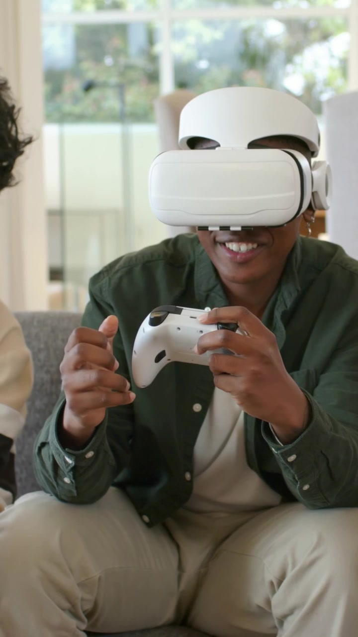 Uomo con visore VR bianco e maglietta verde che gioca con un controller bianco sul divano, sollevandolo.