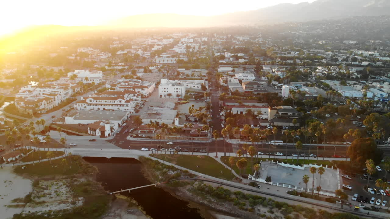 Ripresa aerea con drone che si alza sopra la spiaggia con le palme e i bellissimi edifici e le case del centro di State Street durante il tramonto a Santa Barbara, California.