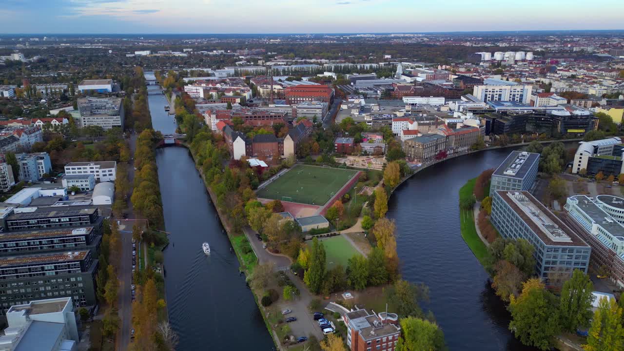Berlin cityscape featuring a river, urban buildings, and a soccer field during autumn. Perfect aerial view flight drone top down Above view
