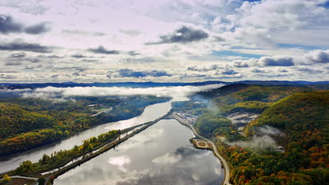 river flowing between the picturesque rocky banks covered with lush greenery. multiple clouds cover the sky above the waterscape. top view.