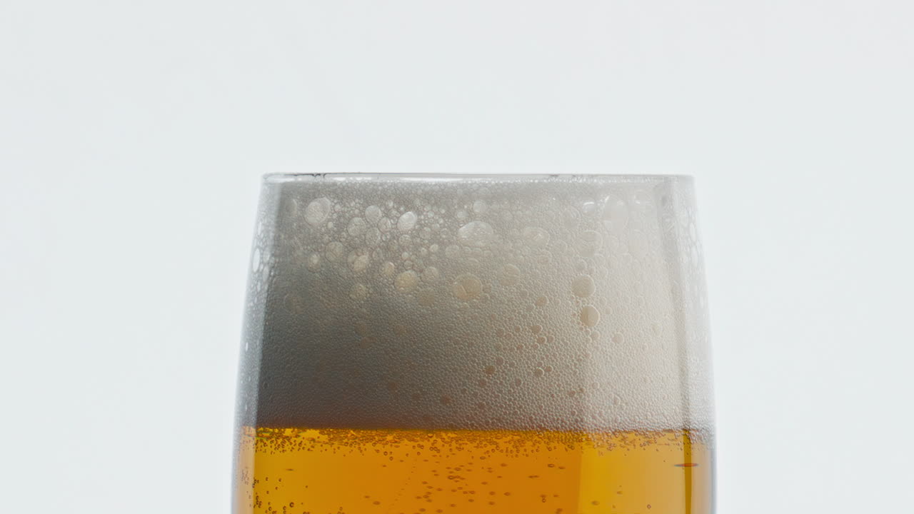 Calice di birra schiumosa statico, sfondo bianco. Texture di bevanda alcolica con bollicine, primo piano.