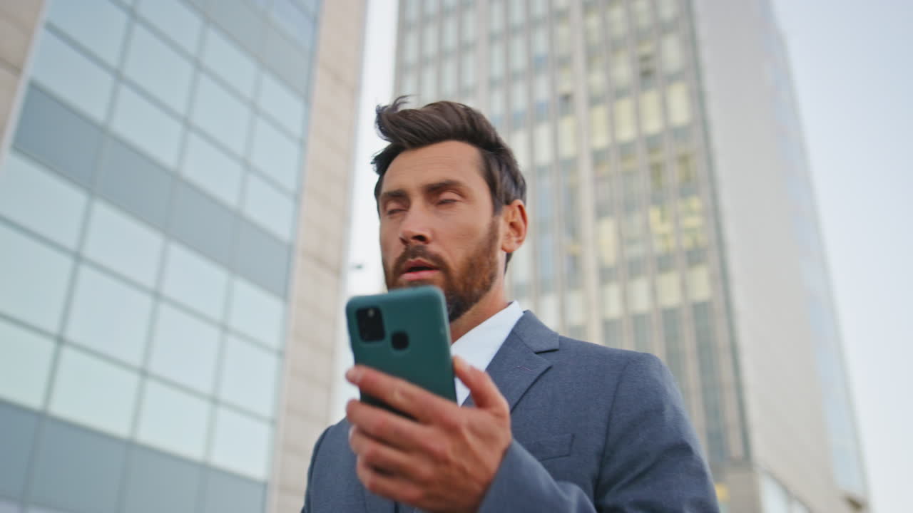 un hombre de negocios caminando respondiendo a una llamada de teléfono inteligente en una calle de la ciudad moderna de cerca.