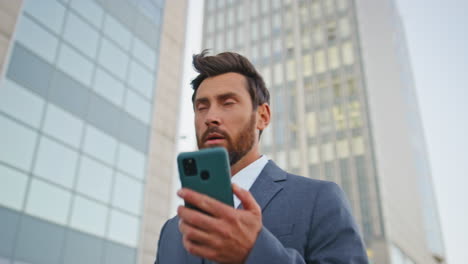 walking businessman answering smartphone call on modern city street close up.
