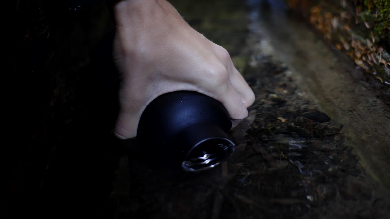 Hand holding a water bottle in a stream
