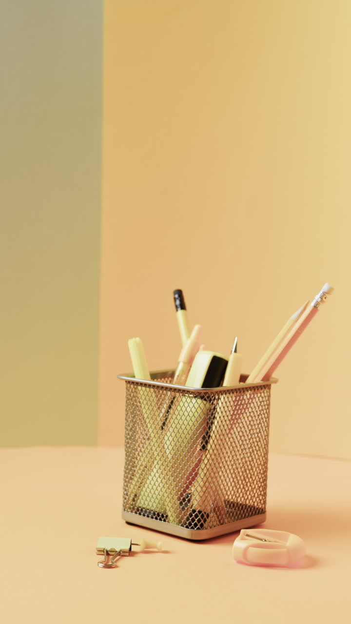 Vertical video of close up of school stationery in cup on yellow background, in slow motion