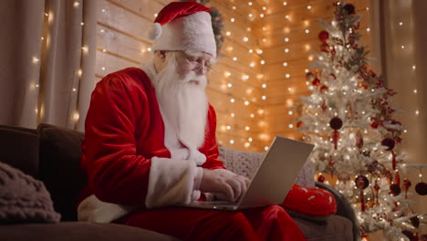 Side-view-Santa-Claus-working-on-laptop-sends-letters-with-wishes-or-congratulations-by-email-for-Christmas-or-New-Year.-Santa-communicates-on-social-networks-with-children-around-world.
