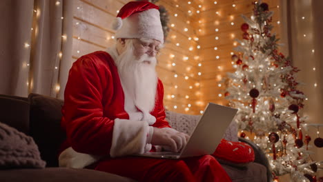 side view santa claus working on laptop sends letters with wishes or congratulations by email for christmas or new year. santa communicates on social networks with children around world.