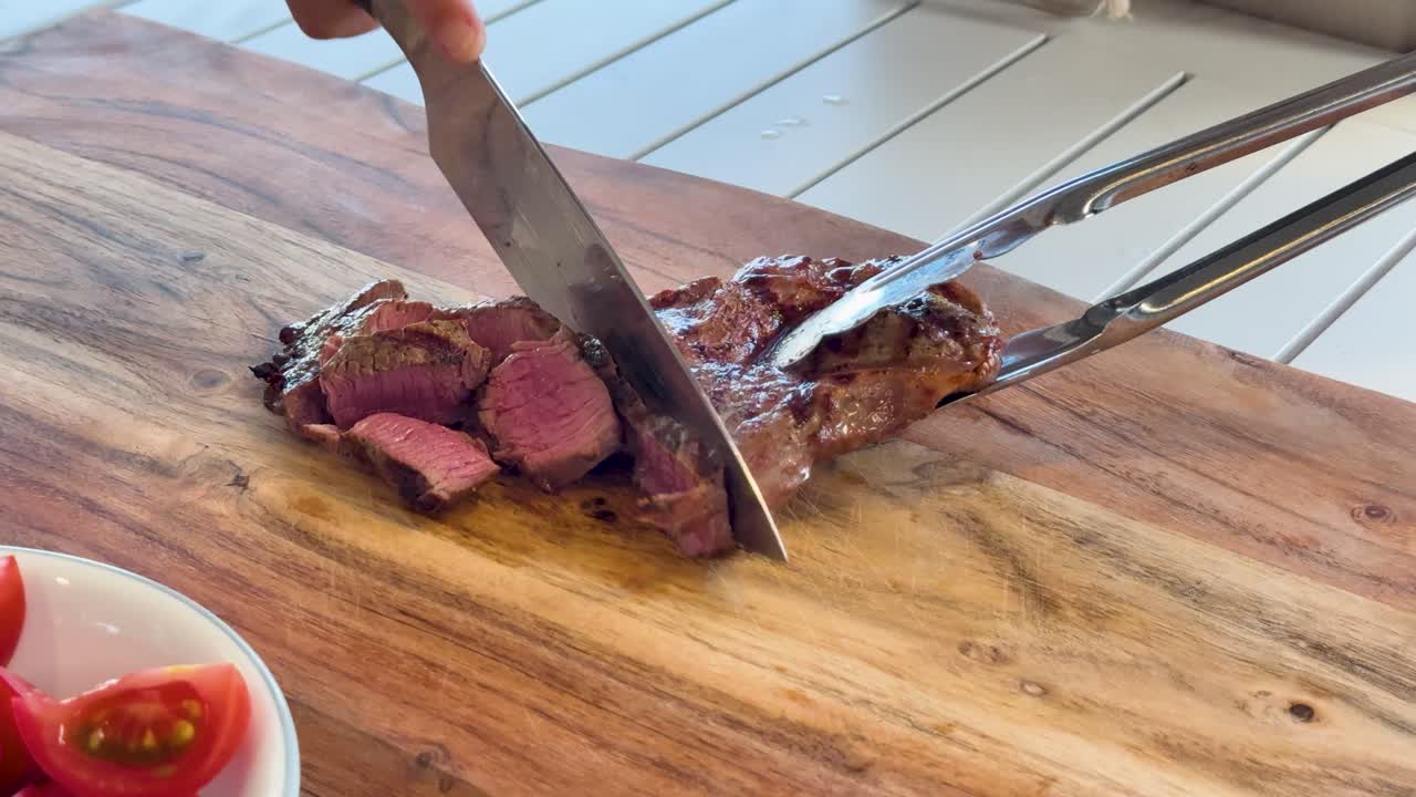 A hand uses a chef’s knife and tongs to slice a juicy, medium-rare Wagyu steak on a wooden cutting board in bright, natural light