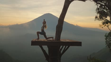 mujer practicando la pose guerrera en una plataforma de madera con el monte agung en segundo plano