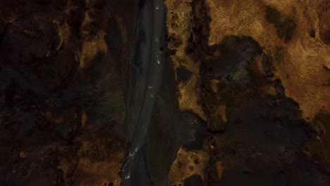 Aerial-top-view-of-a-river-flowing-between-Iceland-highlands-and-volcanic-black-sand