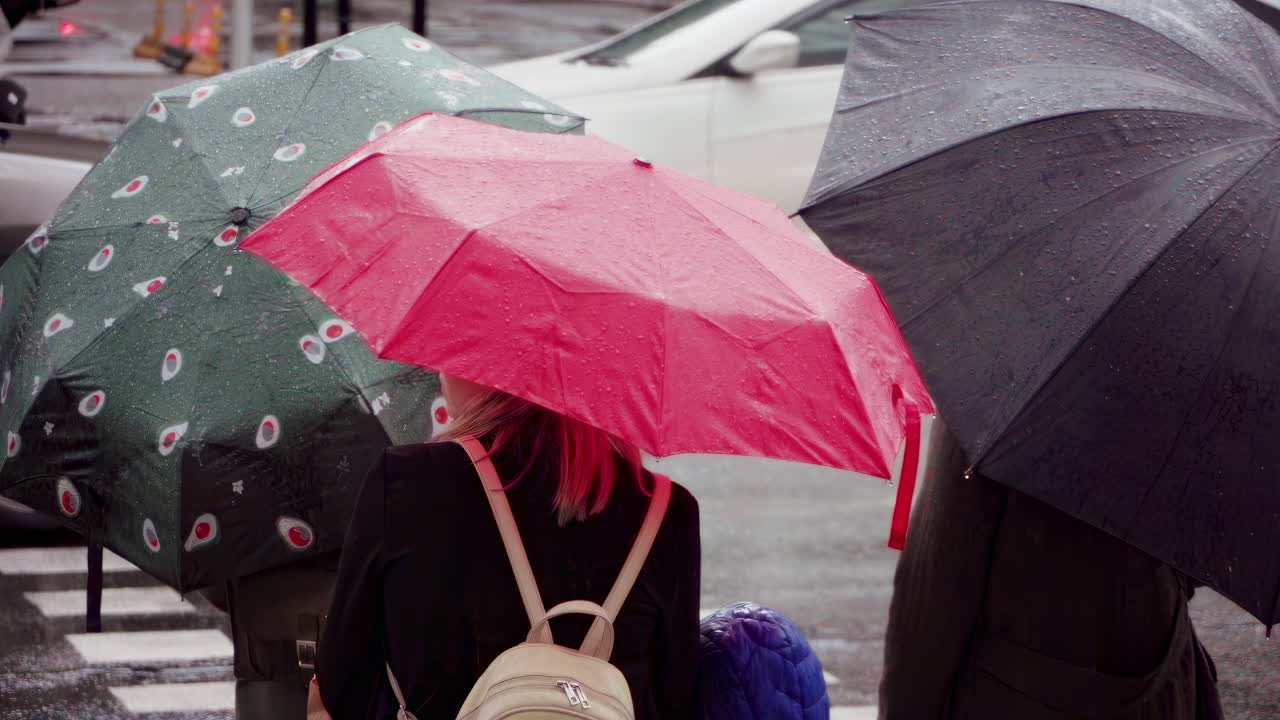 People with umbrellas waiting to cross the street in the rain