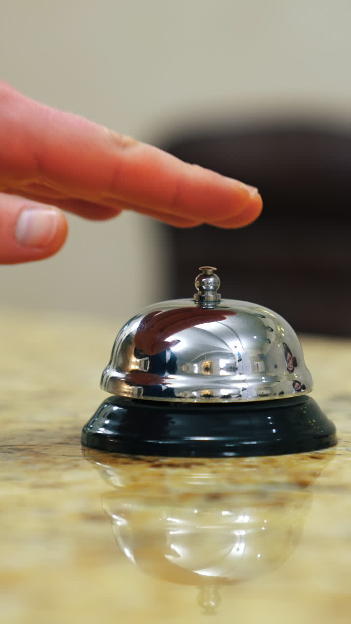 Calling the receptionist. Hand of a tourist in the reception of a hotel presses the bell button. Close-up. Vertical video