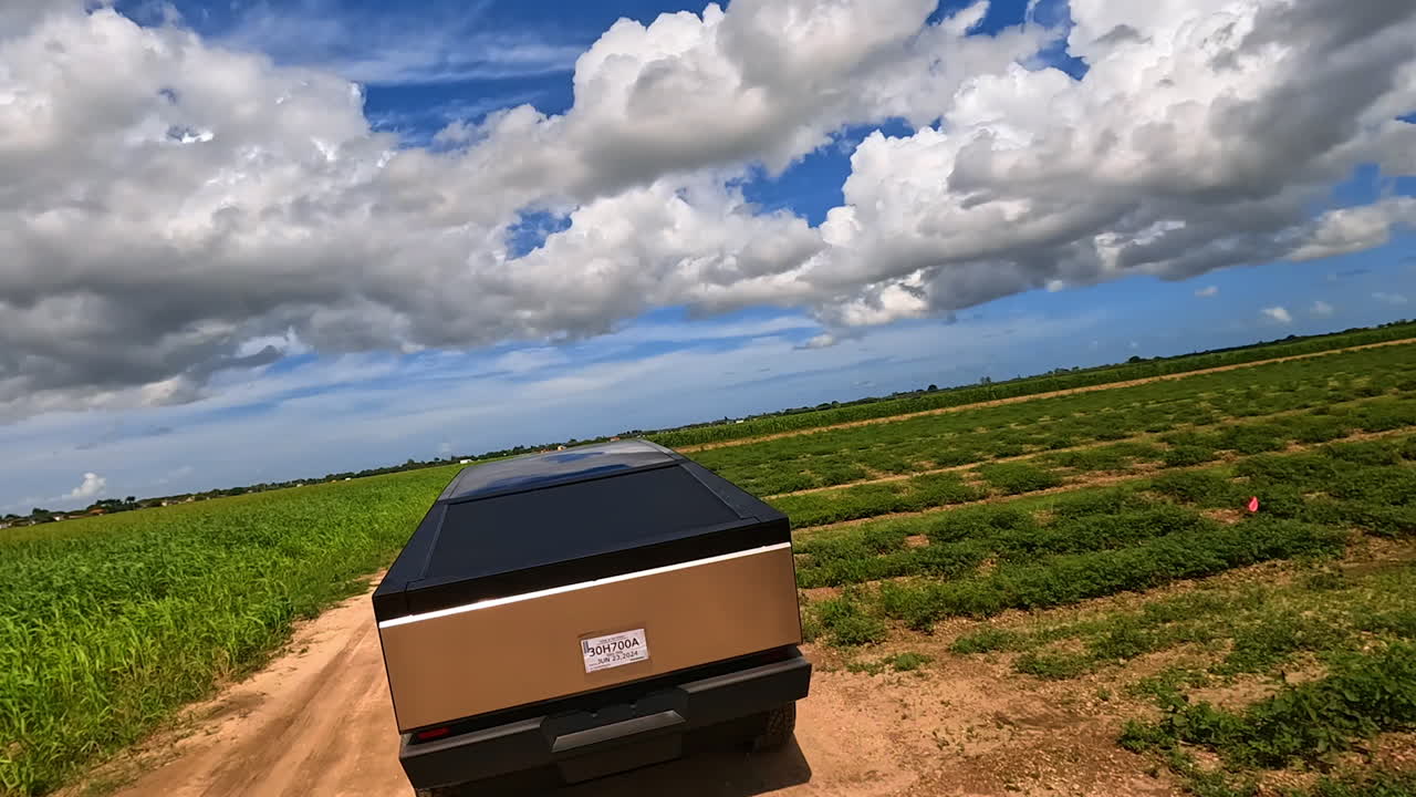 Futuristic Tesla Cybertruck ride outdoors on sunny day. FPV drone following the automobile in the field.