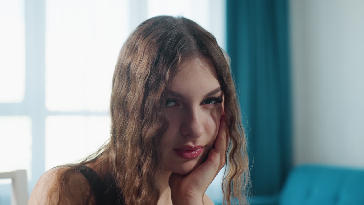 Reflective Female Relaxes On Couch, Contemplative Woman Sitting Quietly By Window With Blue Curtain, Pensive Caucasian Female Reclining Thoughtfully On Sofa Near Natural Daylight And Blue Drape