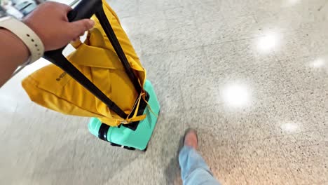 hand holding suitcase handle and yellow bag in airport