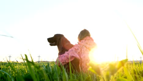 woman hugging the dog at sunset while sitting on the grass