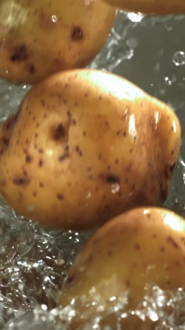 Patate fresche che si tuffano in acqua pulita al rallentatore