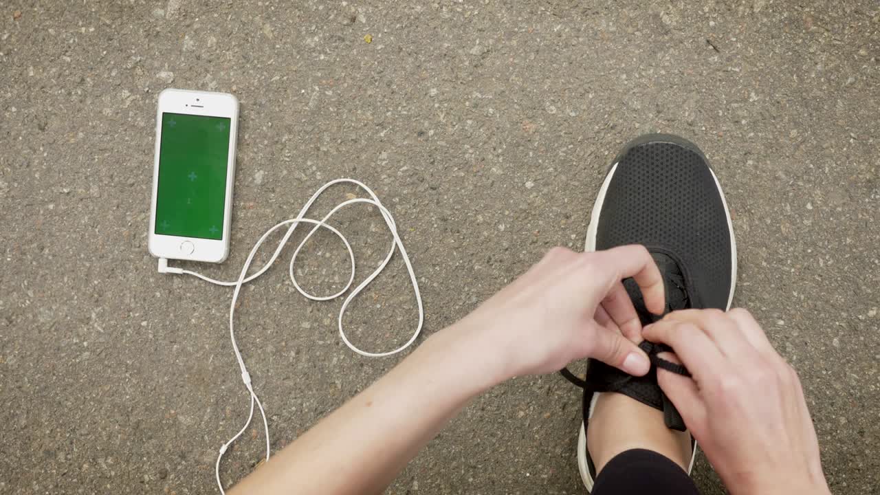 여자 스포츠맨은 스마트폰과 헤드폰이 바닥에 놓여있는 동안 신발을 습니다.