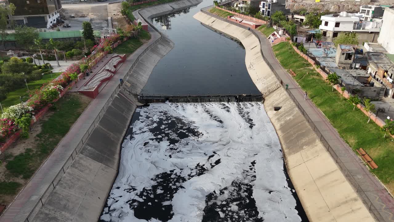 Captura aérea de un perro pasando por el denso desarrollo urbano de Jaipur, donde corren las aguas residuales.