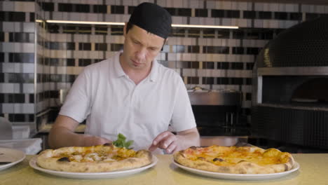 front view of a chef placing basil leaves on baked pizzas