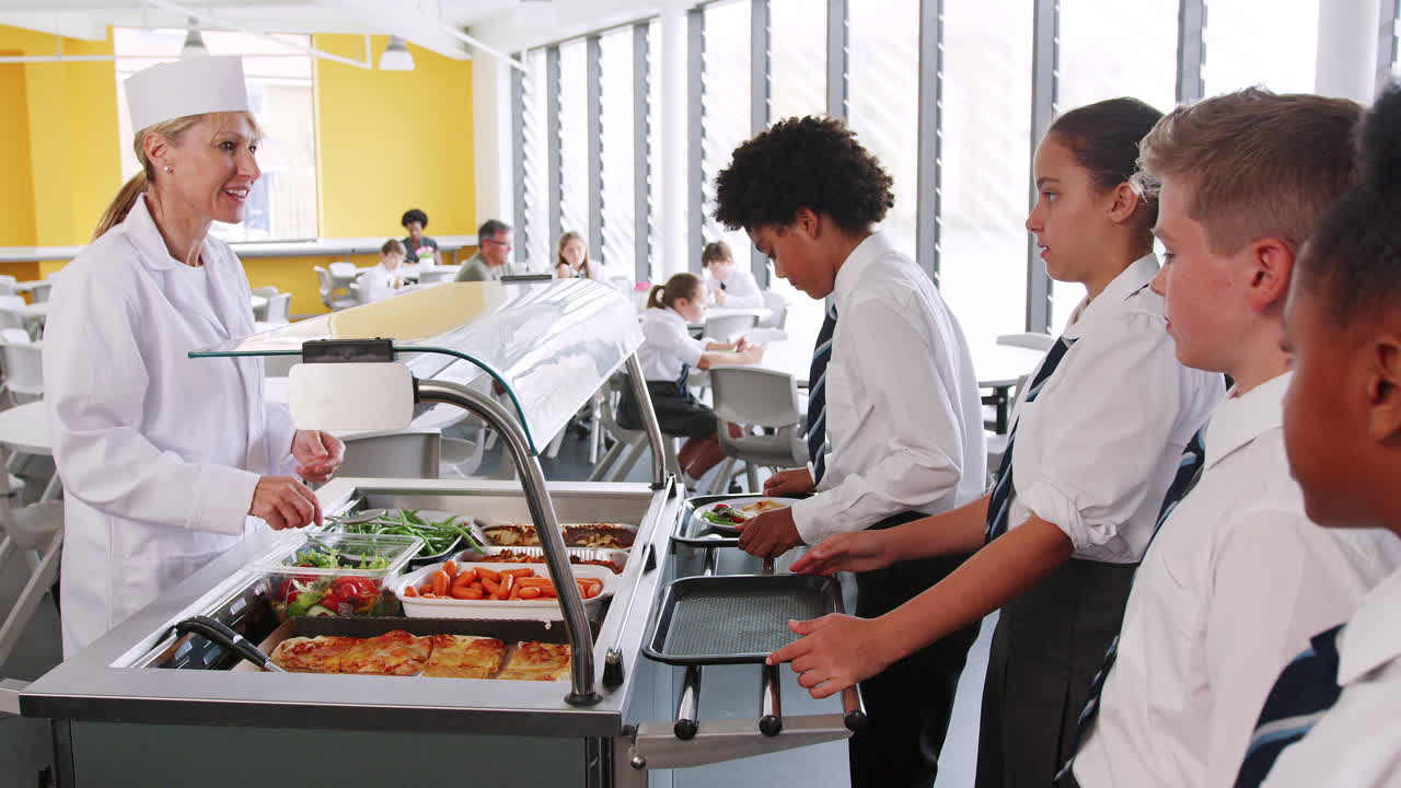estudiantes de secundaria vestidos con uniforme siendo servidos alimentos en la cantina