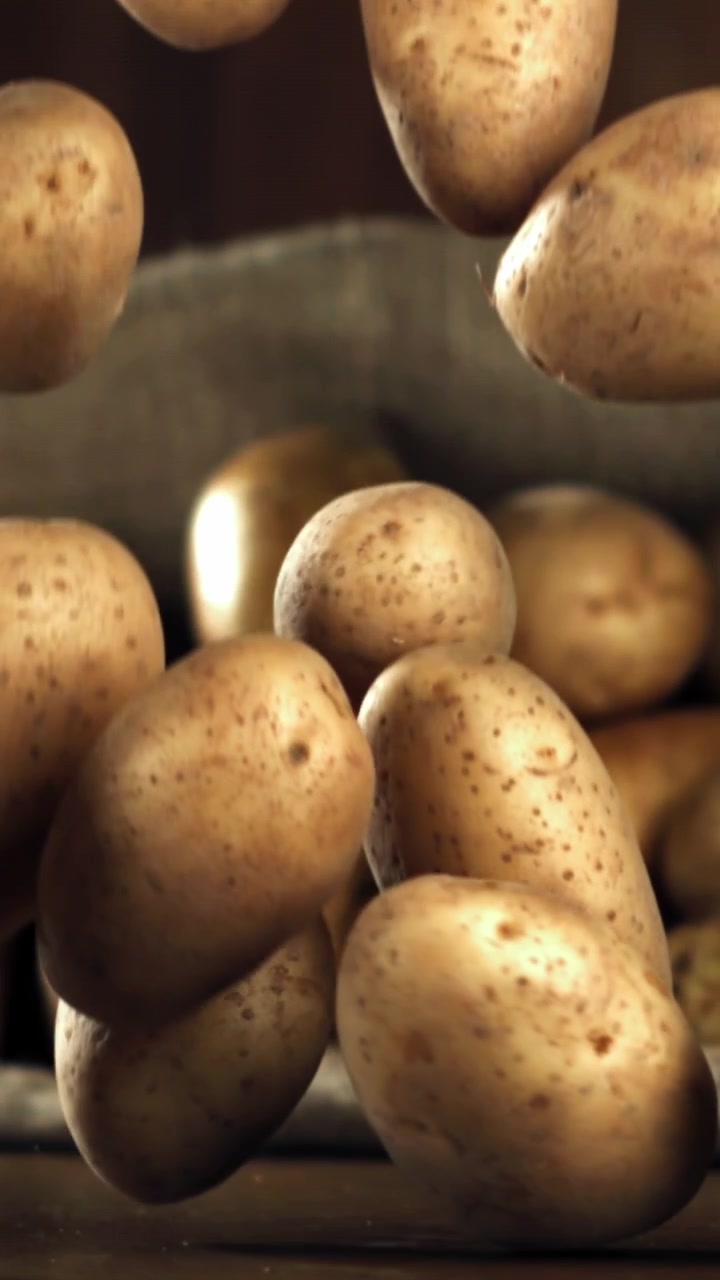 Patate crude che cadono al rallentatore su un tavolo di legno