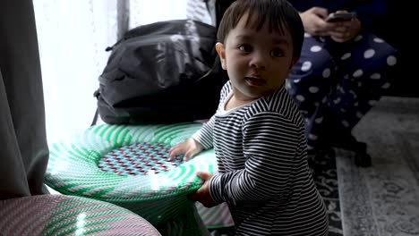 adorable 8 month old boy standing up beside woven rattan stool