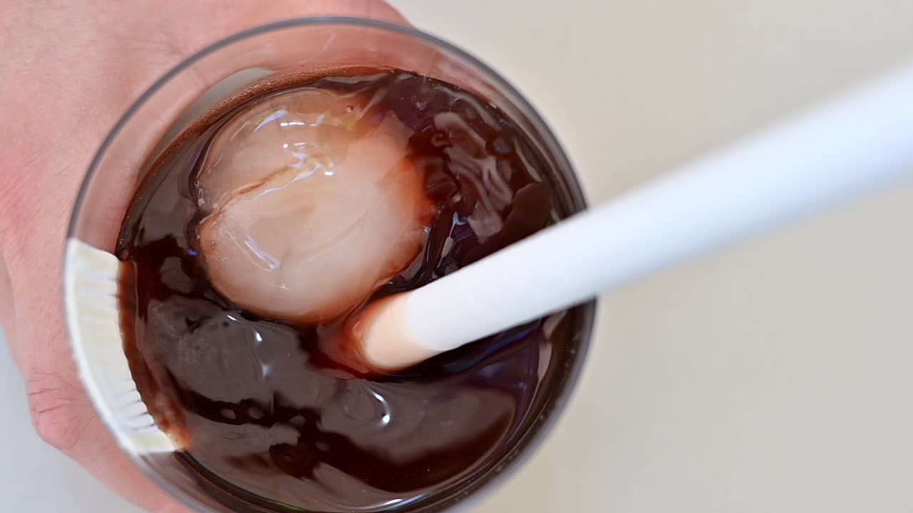Woman hand shaking cold brewed coffee with ice, slow motion close up