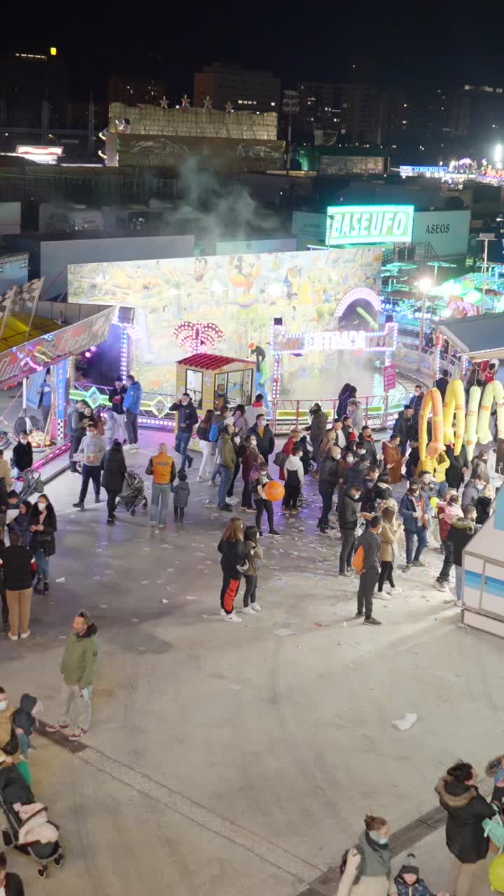 Night view of a lively outdoor market or amusement park with a large crowd of people and brightly lit stalls
