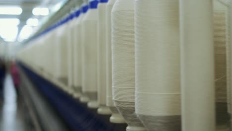 close-up of large bobbins with cotton threads moving along the conveyor