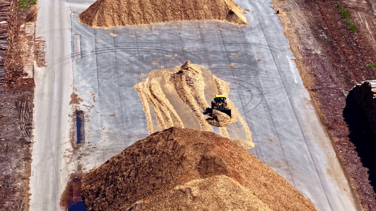 Loader moving wood chips at timber processing yard on sunny day in aerial view