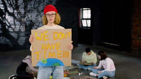 Serious-young-environmental-activist-holding-a-cardboard-with-We-don't-have-time"-inscription-and-looking-at-the-camera"