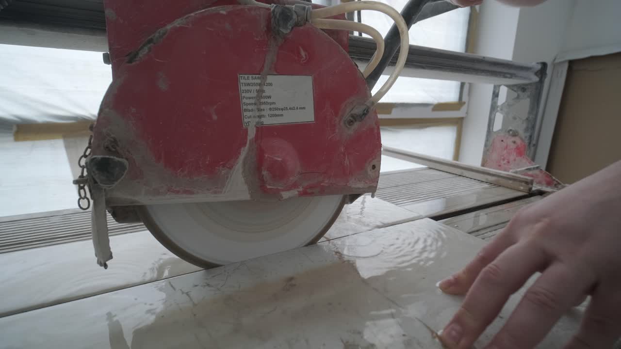 Close-up of a worker's hands guiding a ceramic tile through an electric wet saw, capturing the precision and skill in tile cutting