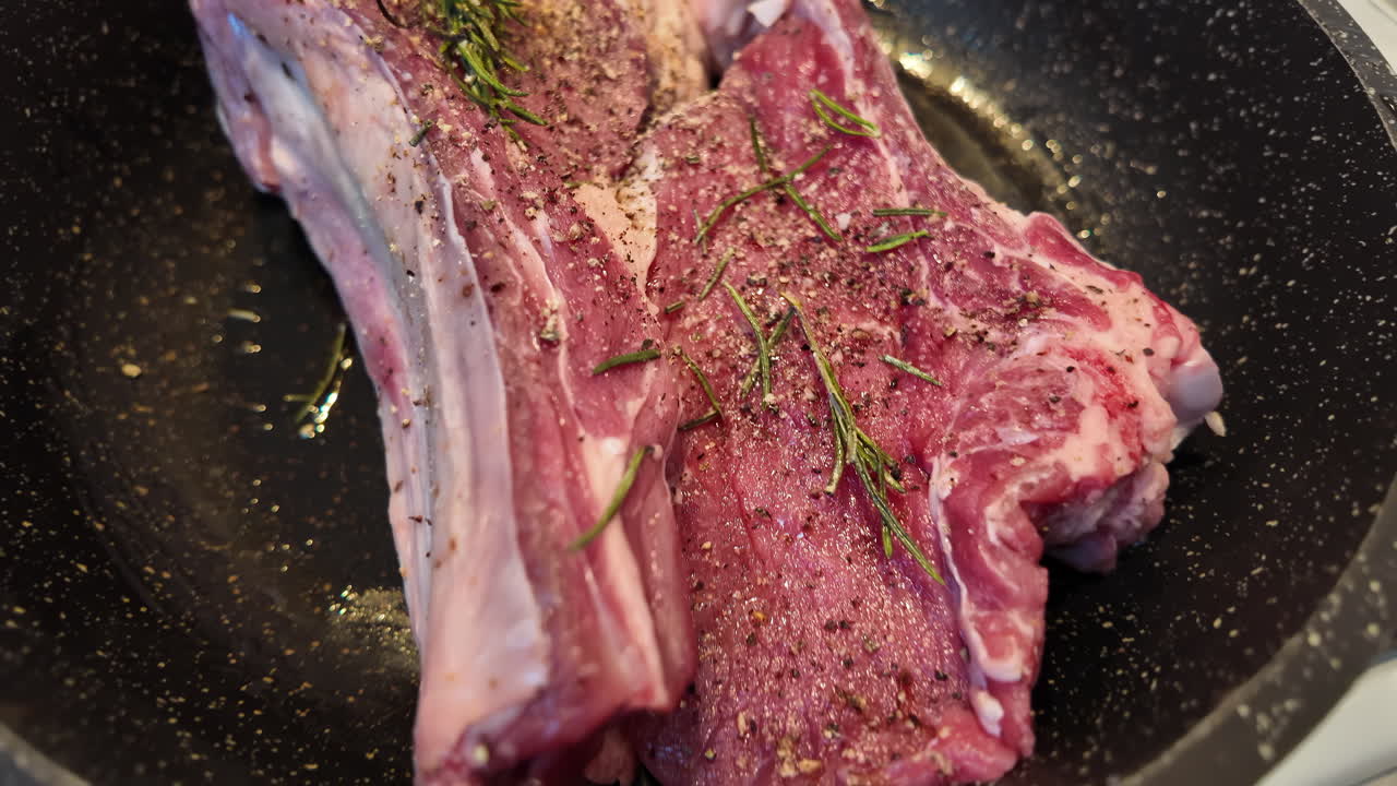 Big red beef stake on a black pan with rosemary ready for cooking, black pepper on top