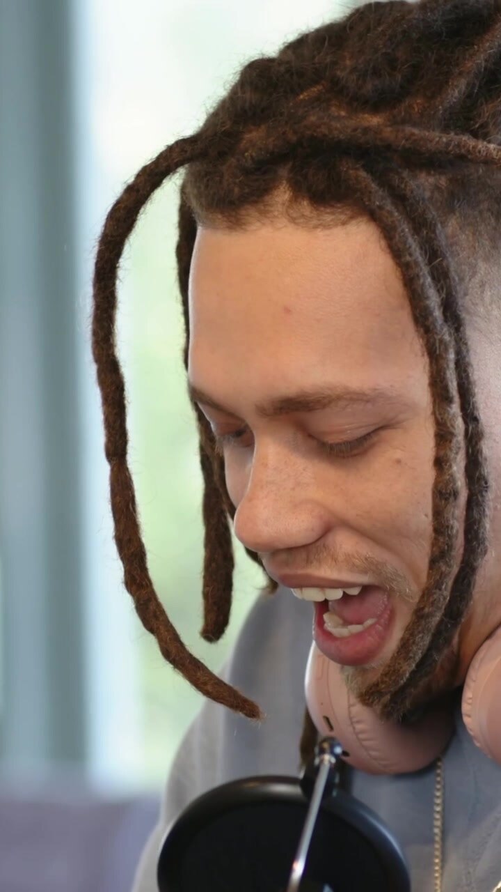 Vertical video: Adjusting mic, man with dreads leaning in and recording podcast at home studio