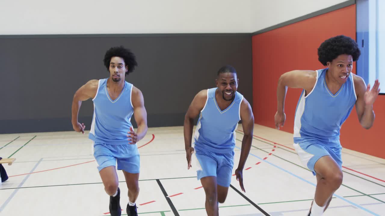 Happy diverse male basketball team training, sprinting on indoor court, slow motion