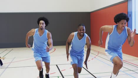 happy diverse male basketball team training, sprinting on indoor court, slow motion