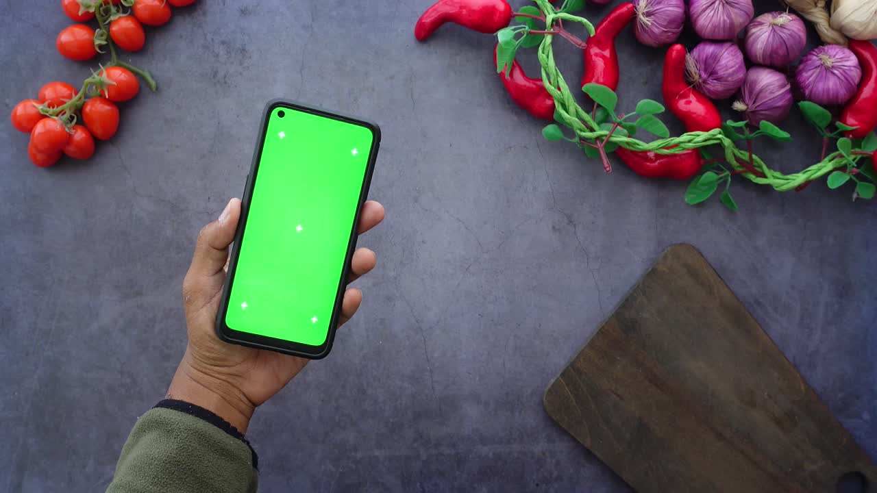 Overhead shot of a smartphone with a green screen surrounded by fresh produce