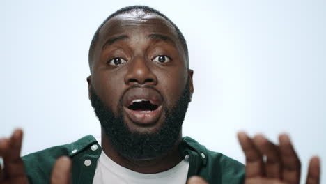 Portrait of shocked african guy looking at camera in light background.