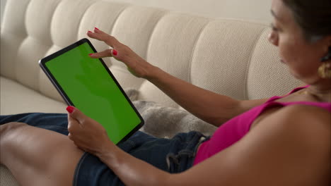 movimiento lento de una mujer latina mexicana con una camiseta rosa acostada en su sofá desplazándose navegando por su tableta con su dedo índice hacia arriba