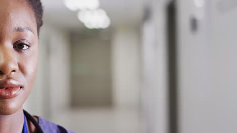 Half-face-video-portrait-of-smiling-african-american-female-doctor-in-corridor,-with-copy-space