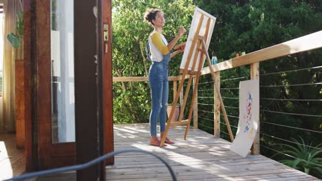 mixed race woman painting on canvas in the balcony at home