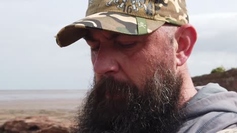 sad bearded urban man wearing baseball cap looking across windy beach