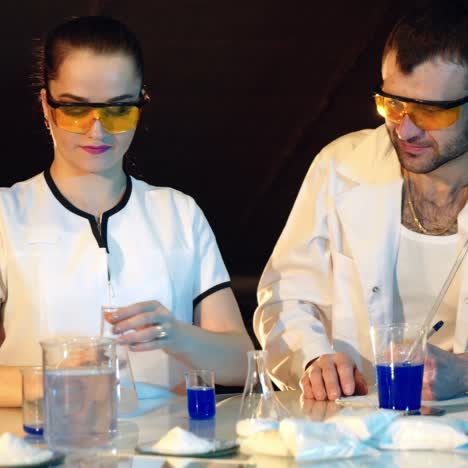 two doctors in eyglasses are experimenting with test tubes with chemicals at a table in the laboratory on a black background
